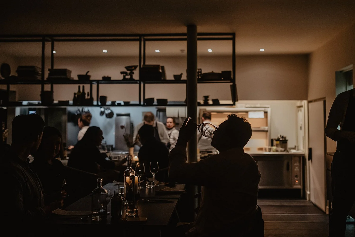 Diners at the counter watching the open kitchen at work in the evening